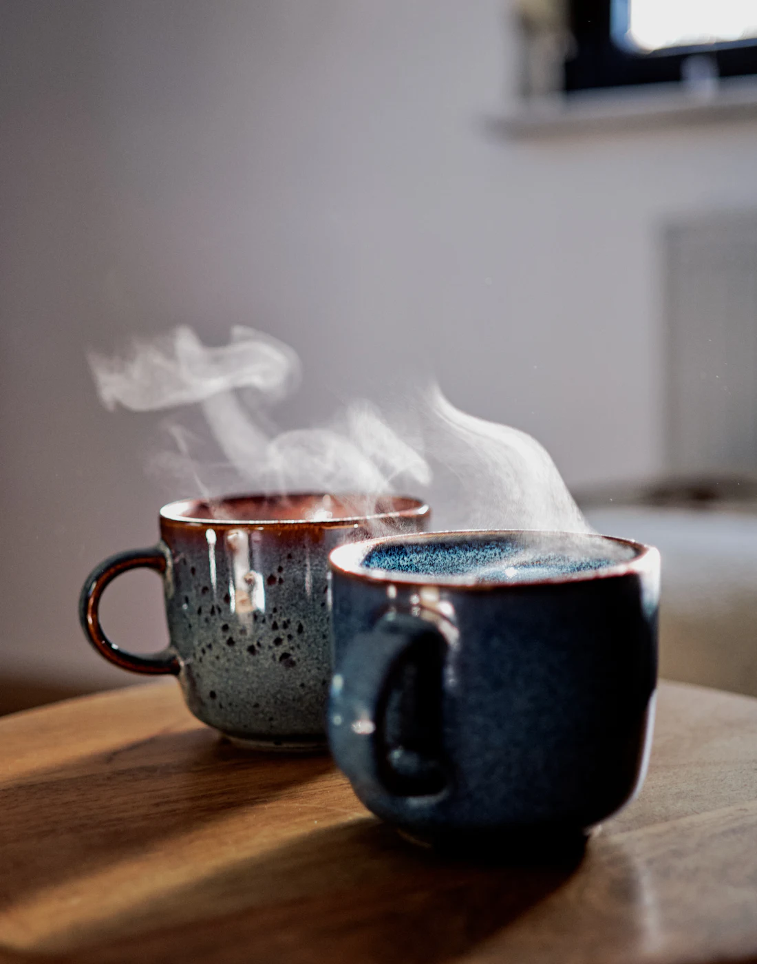 Two cups of coffee steaming side by side on a table in soft morning light